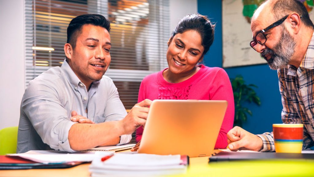 Drei Lehrer erarbeiten im Team ihr Unterrichtsmaterial zusammen an einem Laptop.
