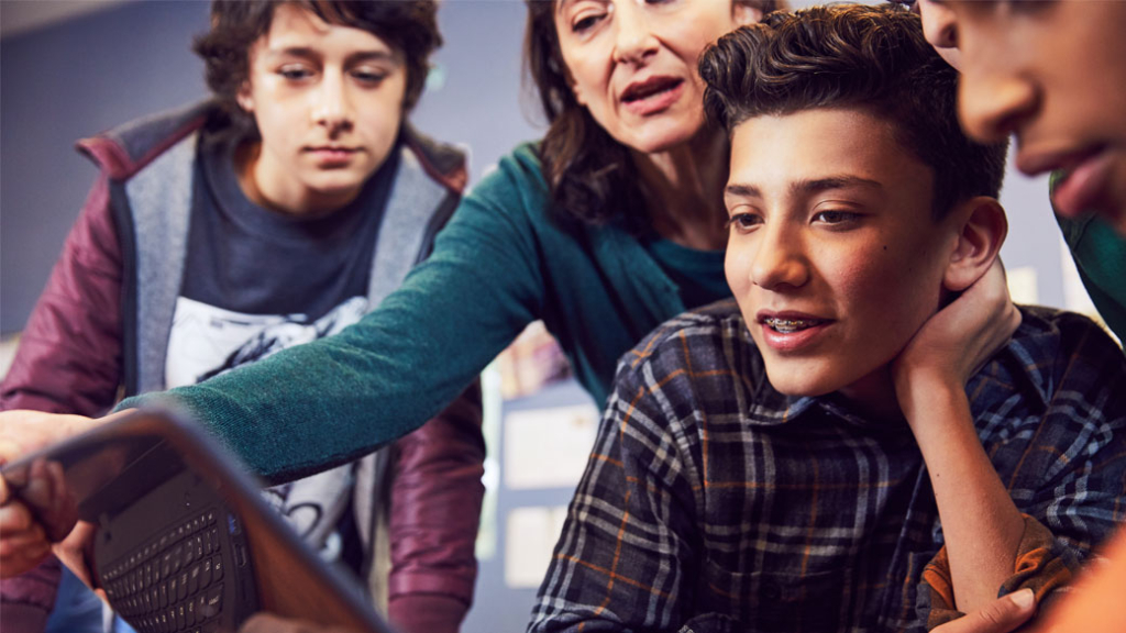 Drei Schüler schauen mit der Lehrerin auf ein digitales Gerät