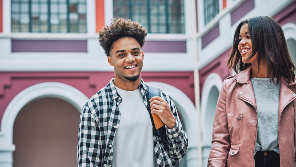 Zwei Studenten laufen über einen Campus und lächeln in die Kamera.