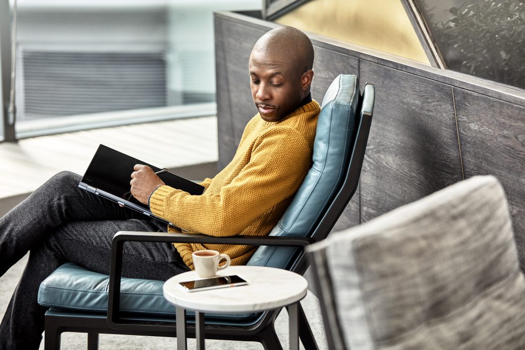 A man is using his Lenovo laptop like a tablet while sitting in a comfortable chair in a Modern office setting