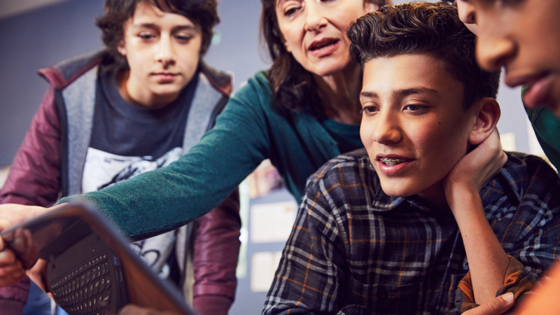 Auf dem Bild sind drei Schüler und eine Lehrerin zu sehen, alle beobachten den Computerbildschirm.