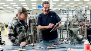 Auf dem Bild sind zwei Männer in einer Werkstatt zu sehen. Ein Mann hält ein Surface in der Hand.