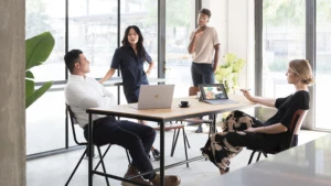 Zwei Frauen und zwei Männer sitzen bzw. stehen an einem Tisch in einem Besprechungsraum mit Surface-Geräten vor ihnen.