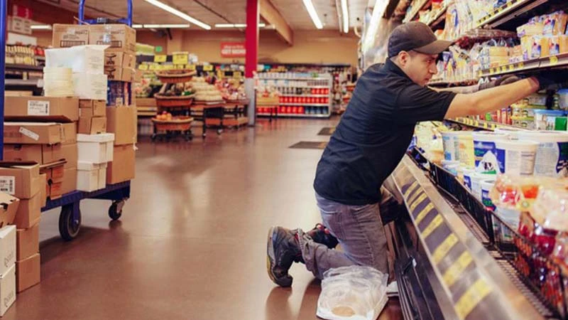 Ein Arbeiter r&auml;umt im Supermarkt ein K&uuml;hlregal ein