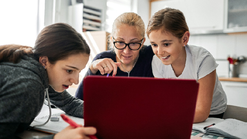 Eine Mutter helft ihren Kindern bei den Hausaufgaben am Laptop