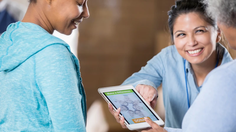 Drei Personen betrachten ein Tablet mit einer Spendenaufforderung. Make a Difference und Spenden-Button sind sichtbar