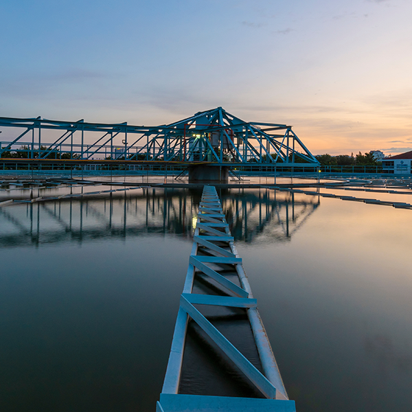 A blue truss structure at the Quincy Water Reuse Utility captured in soft lighting at dawn. The structure rests over water and casts a reflection on the surface.