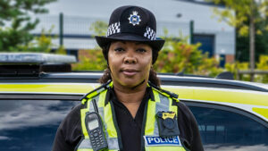 A uniformed police officer standing in front of a marked police vehicle