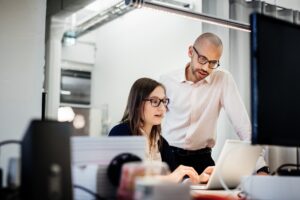 Two professionals collaborating at a desk, reviewing information on a laptop screen in a modern office setting.