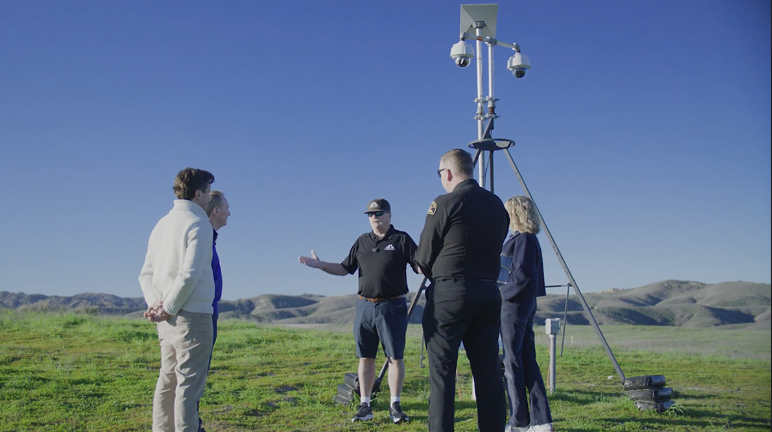 a group of people talking to each other near a tall surveillance camera