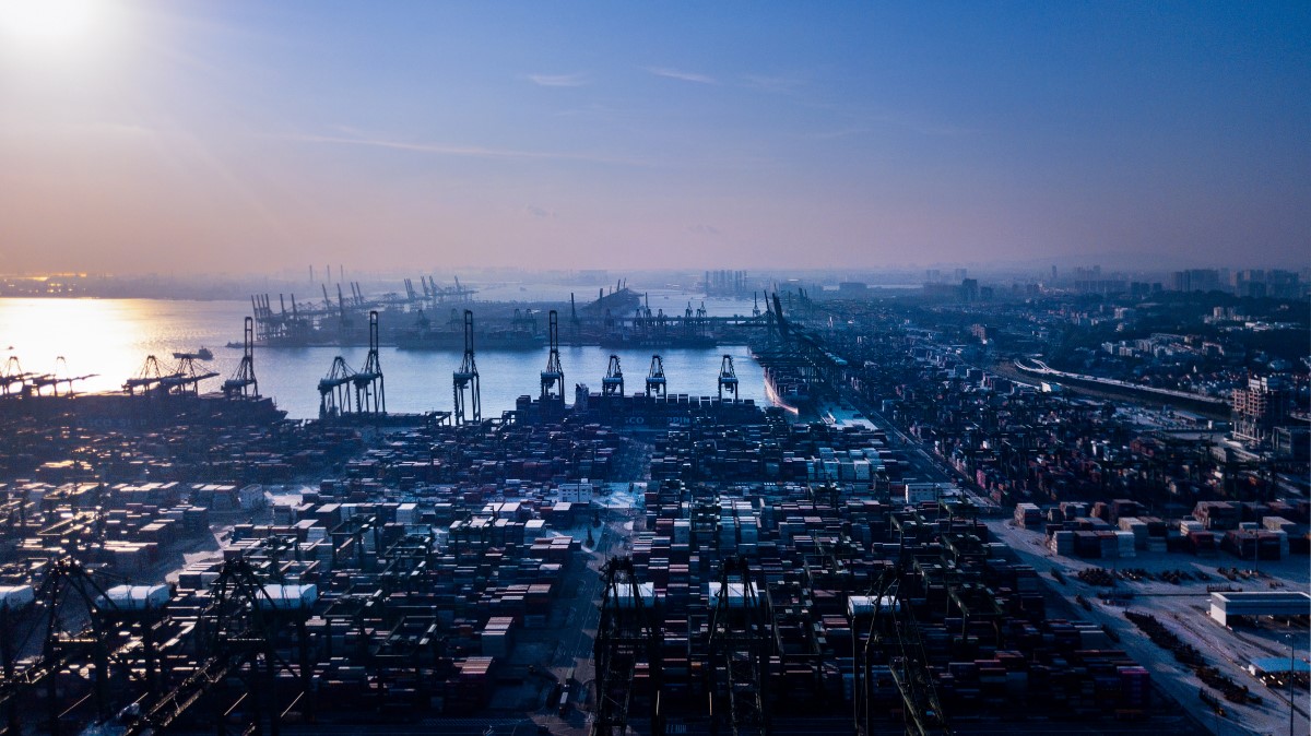 Aerial view of shipyard at Singapore port. Thousands of shipping containers are stacked near cranes lining the water.