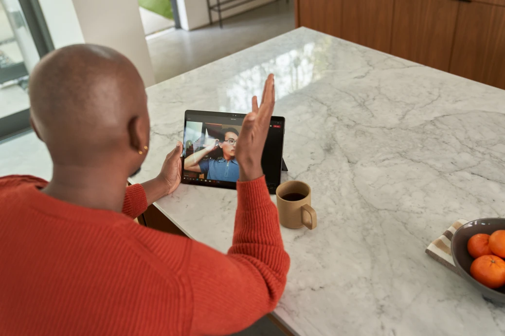 Seller working from home and is on a Microsoft Teams video call. Keywords: Security; Dynamics 365; man; hybrid work; business decision maker (BDM); remote work; manager; end user; Microsoft Defender for Cloud Apps; on the go; Surface tablet; CISO; chief information security officer