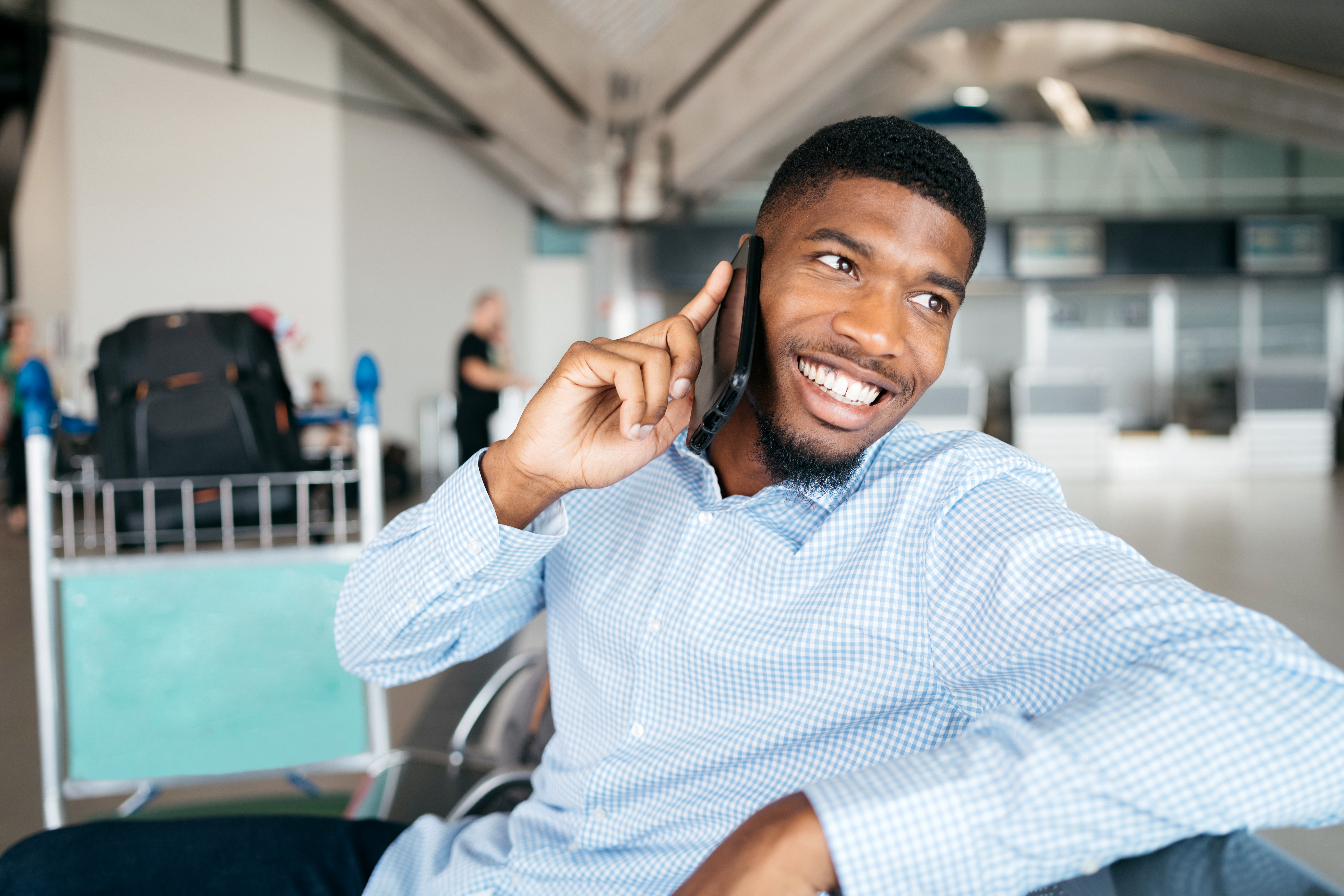 Photo of a smiling young man on the phone at the airport.