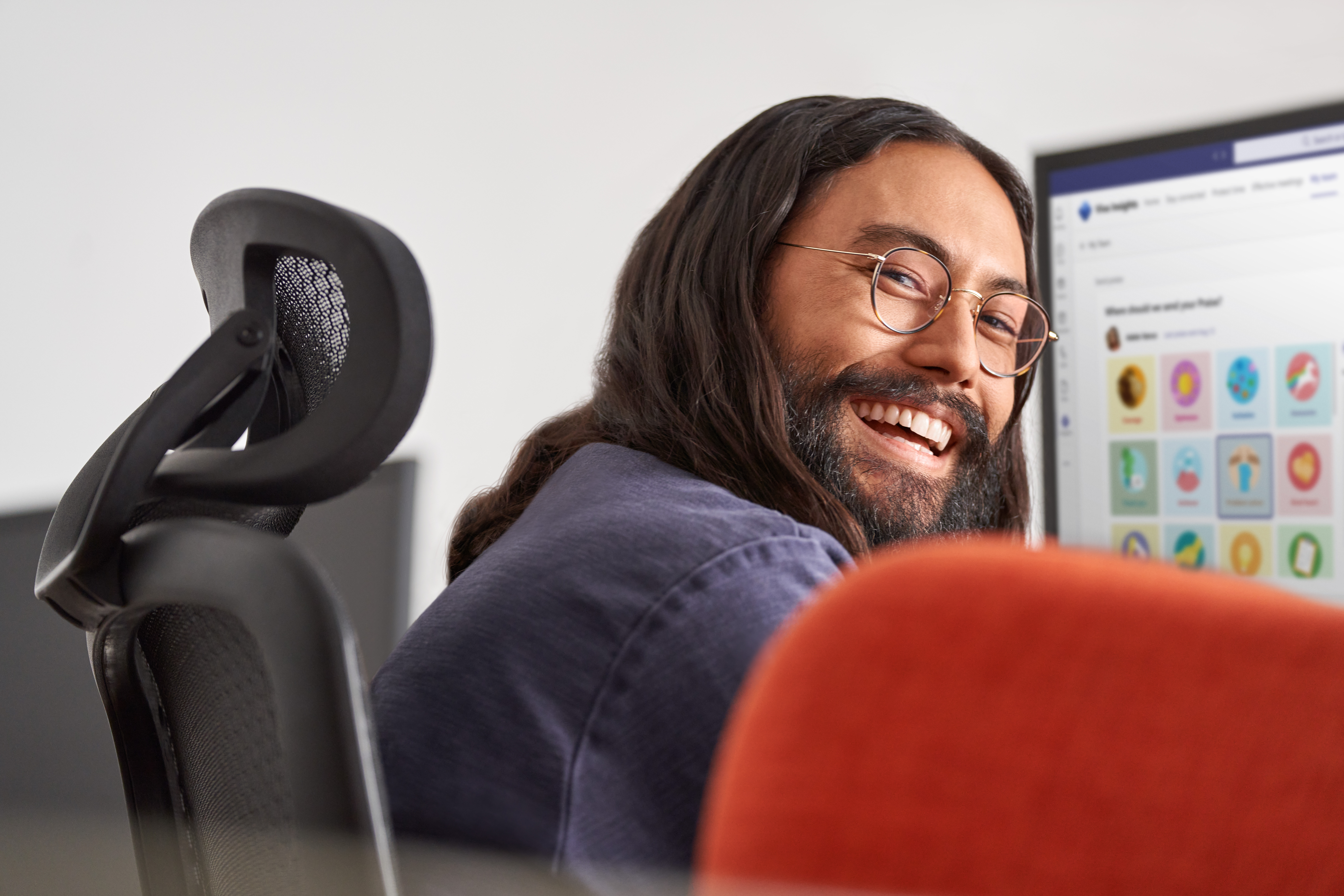 Man smiling while at work​ Keywords: Viva; Filip; hybrid work; work from home; remote; male; desktop monitor; UI screen; glasses; looking back over his shoulder; office; ; Insights; praise