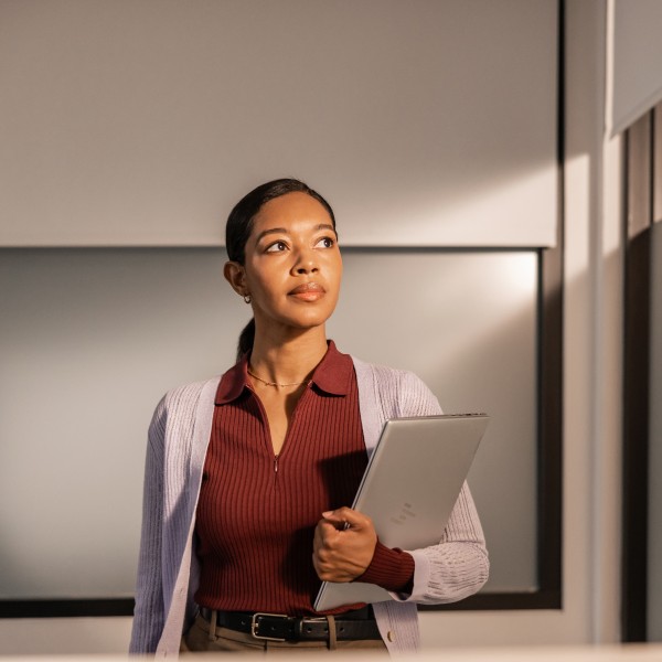 Portrait of woman in a pensive moment of focused work holding a laptop.