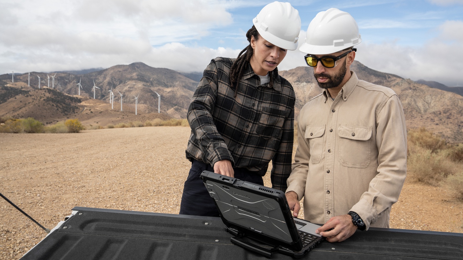 A man and woman wearing hardhats looking at a laptop