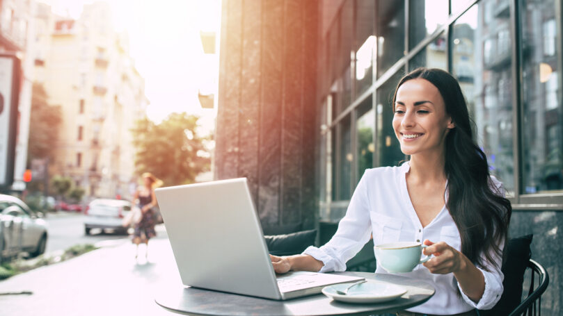 Happy beautiful young businesswoman working on laptop in street cafe outdoor