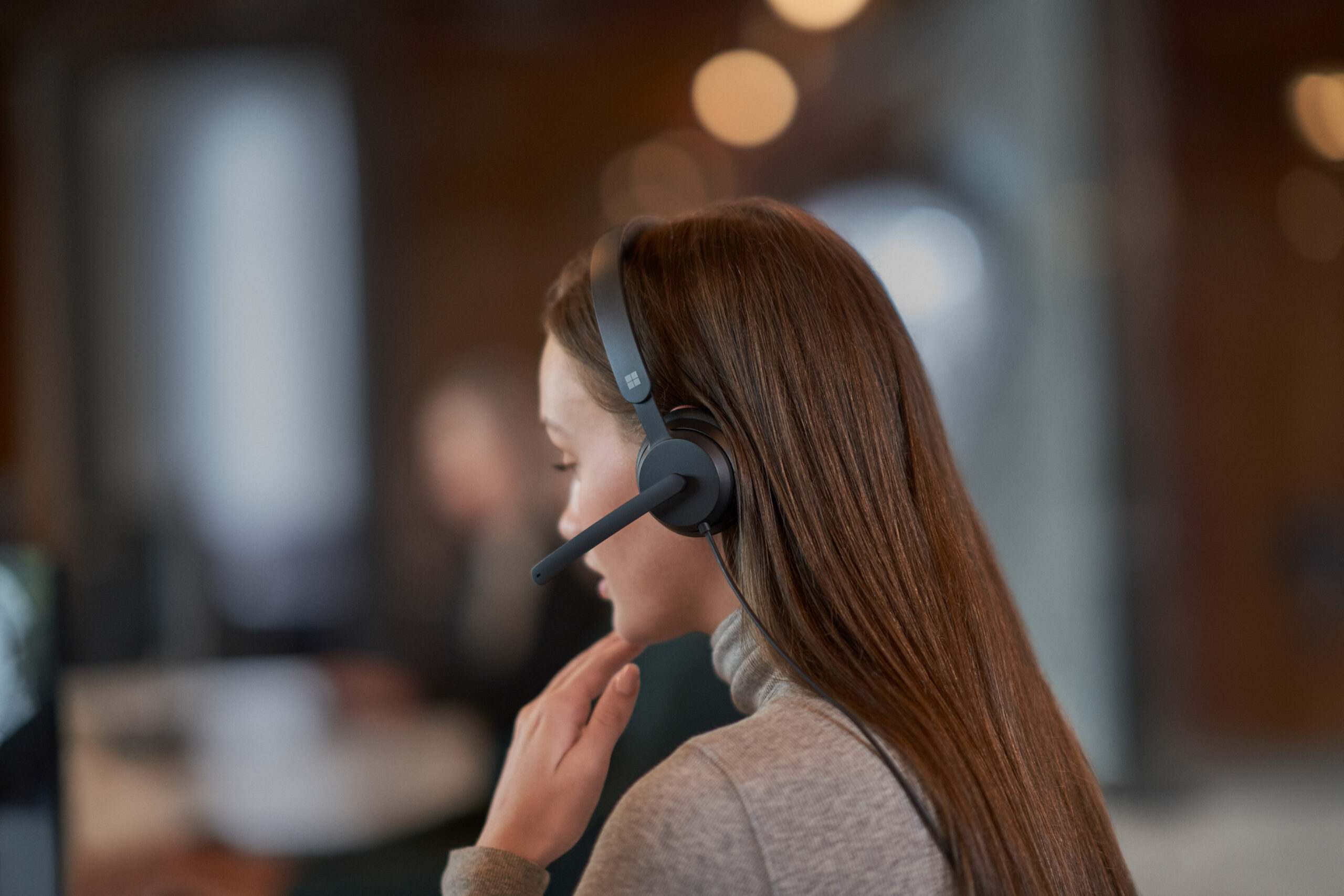“Person wearing a headset, seated at a desk in a modern office environment.”