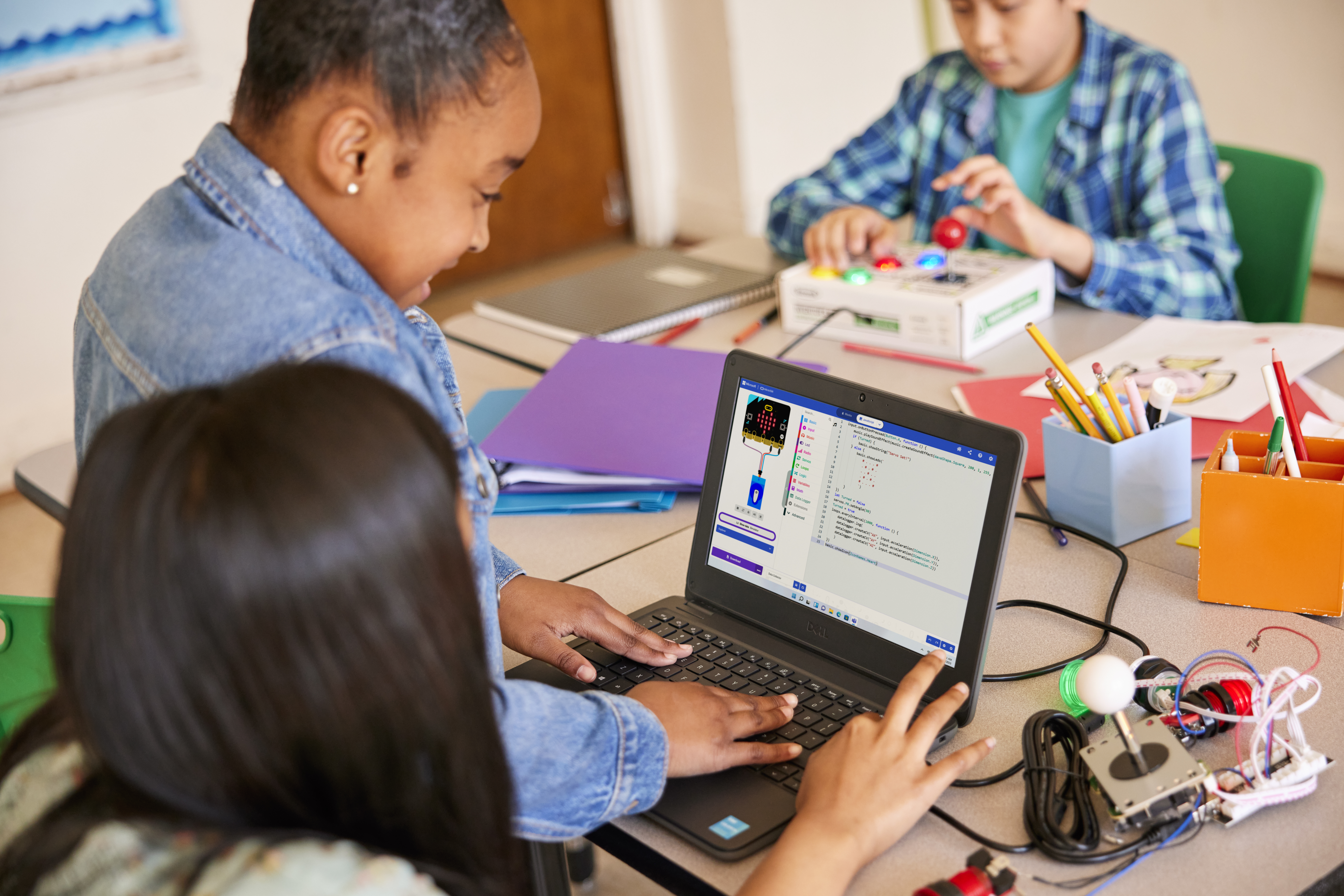 Elementary-aged students working together on a laptop in a school classroom.