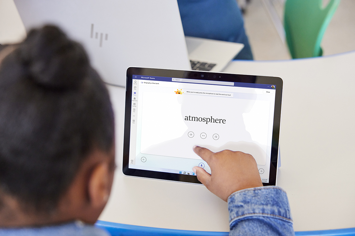 A student sitting at a table in school and interacting with the screen on a tablet.