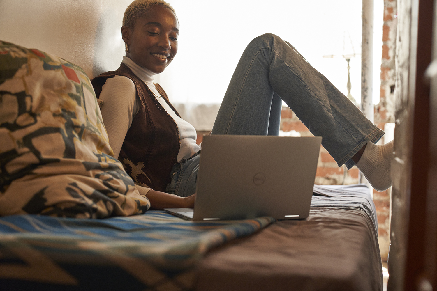 A college student sitting on a bed in a dorm room and working on a laptop.