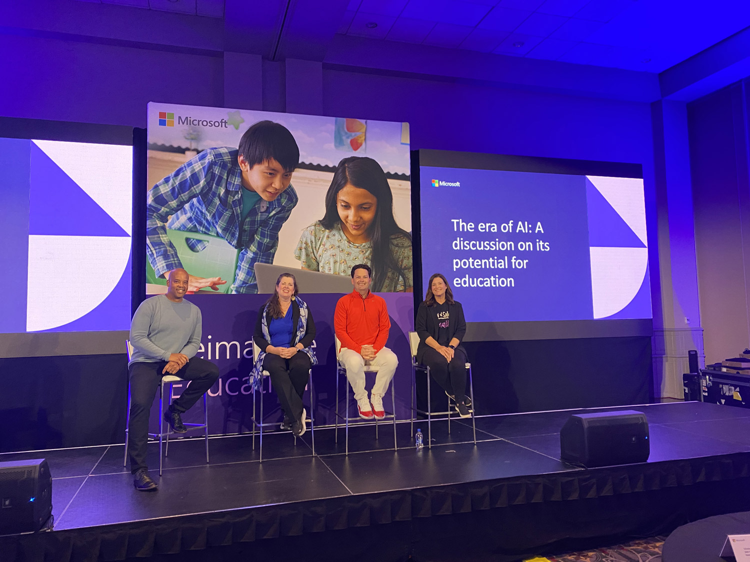 Four people on stage presenting during a session at a conference.