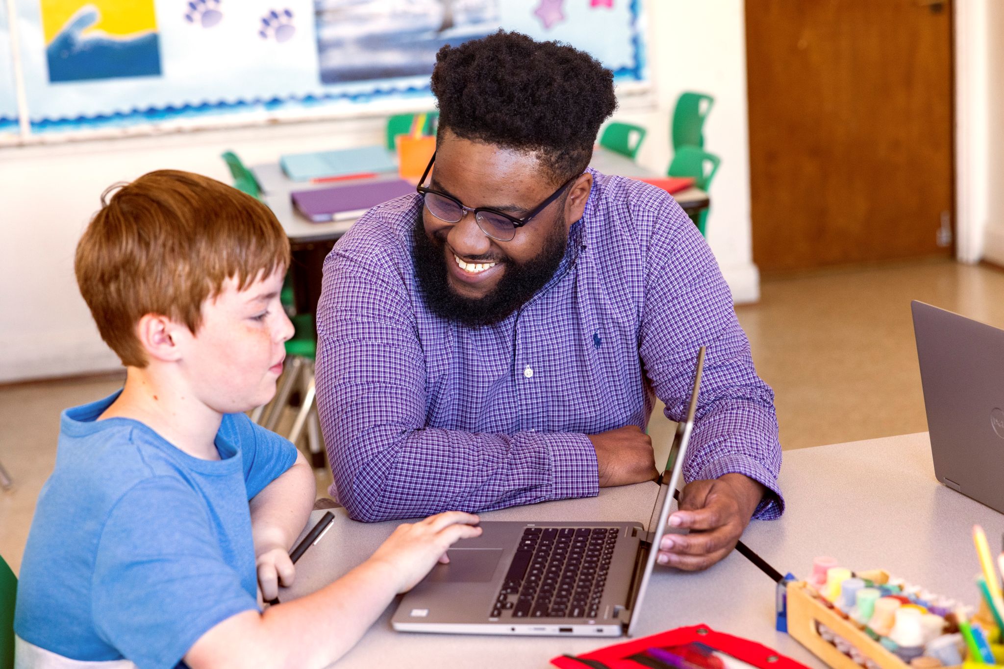 An educator engaging with a student at the student’s desk in a school classroom.