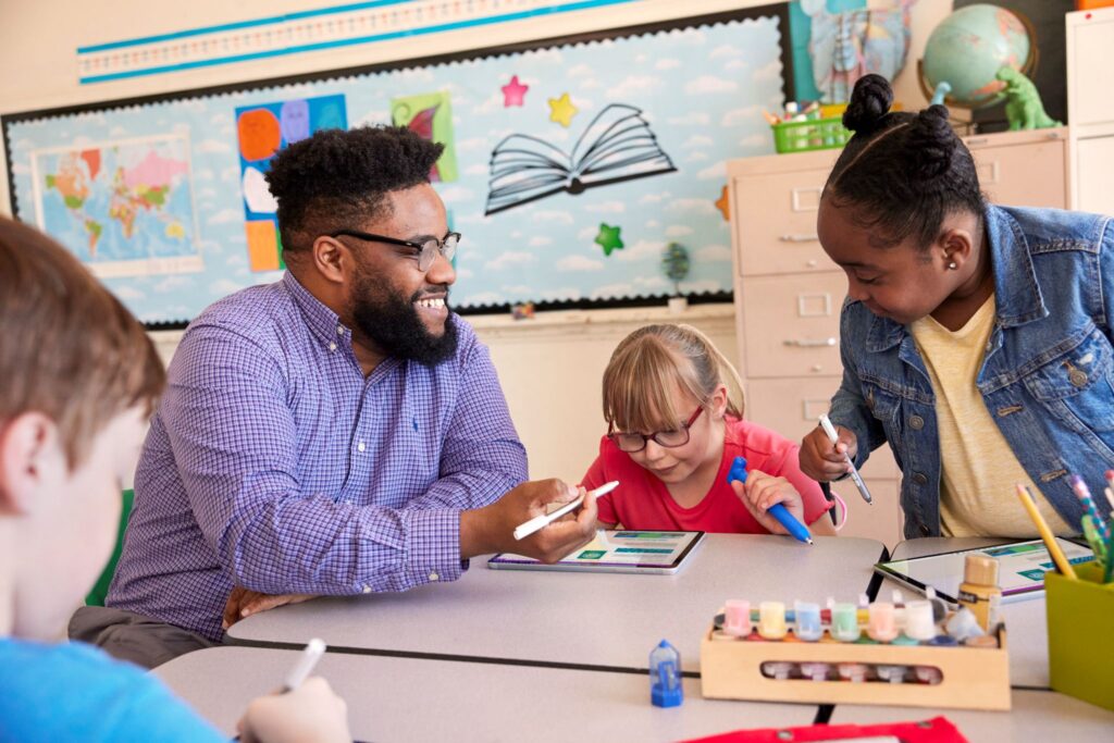 A lighthearted classroom scene with an educator and students working at a cluster of desks.