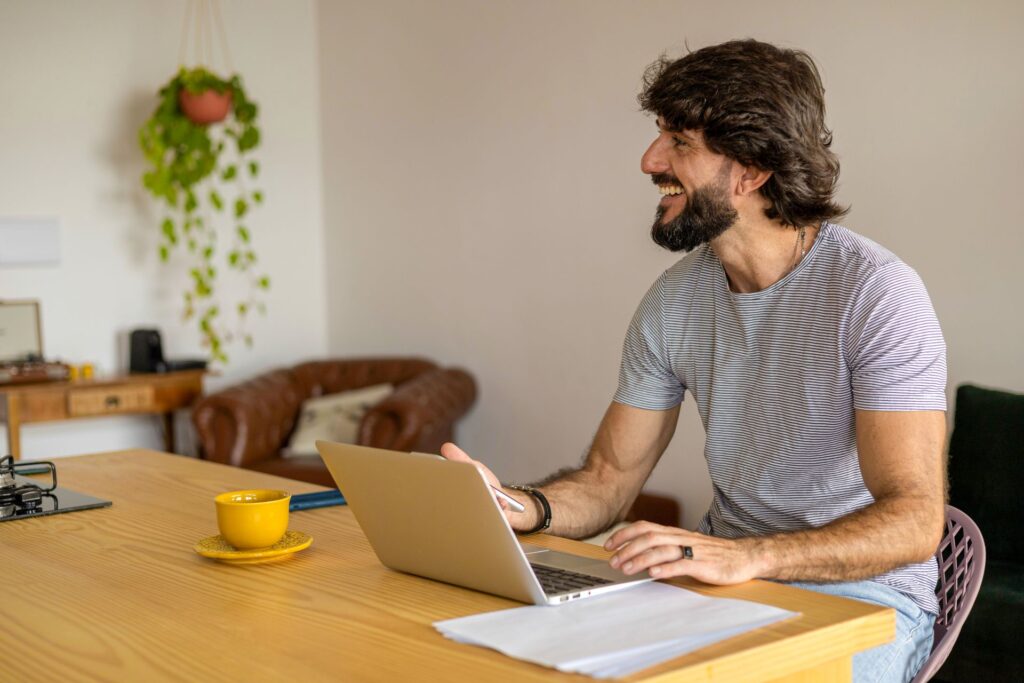 An educator sits at a dining table while working on a laptop.