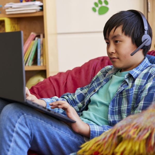 A student wearing headphones in a classroom setting and working independently on a laptop.