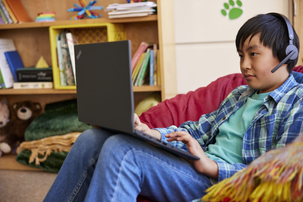 An elementary school student using a laptop and headphones in a classroom setting. 
