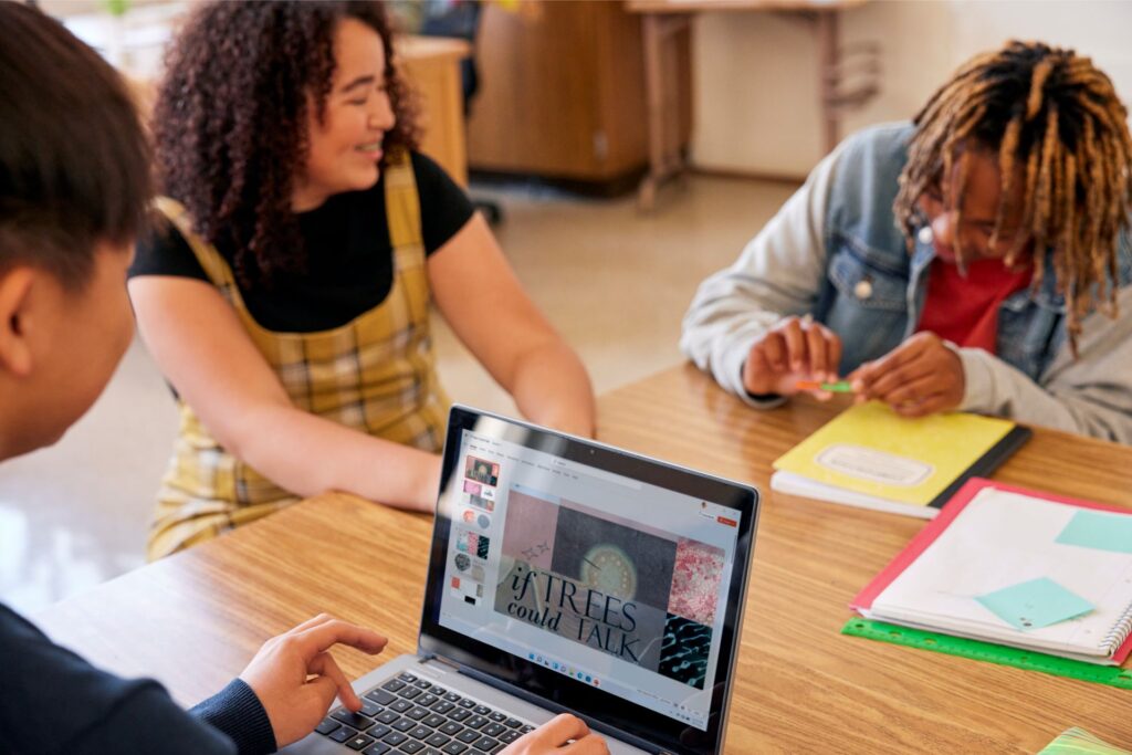Three students working together on a laptop in a school classroom.