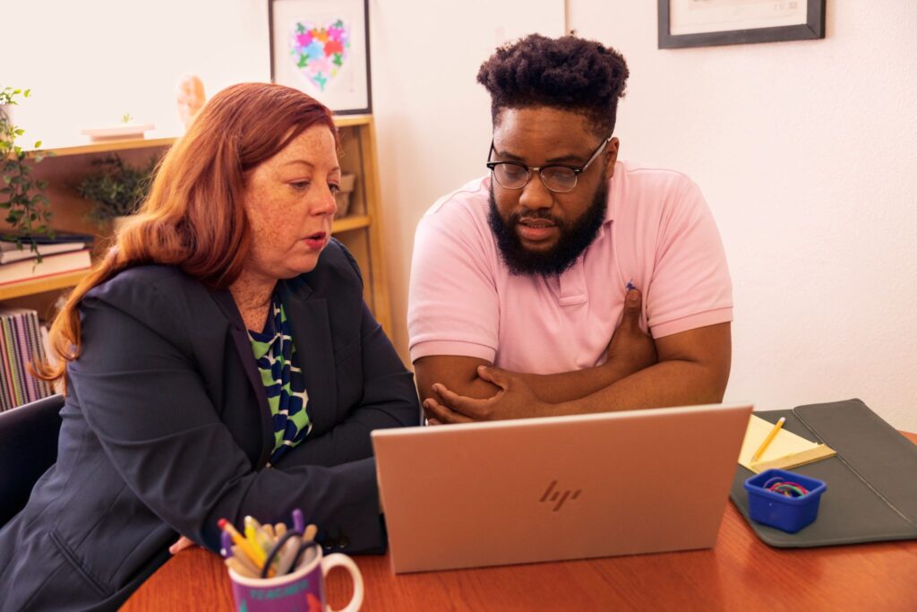 Two educators sitting at a table and looking at the screen of a laptop together.