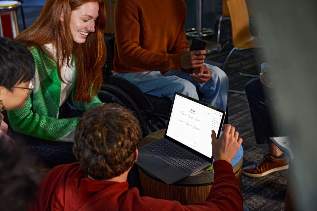 A group of older students sit informally and use Copilot Chat on a laptop.