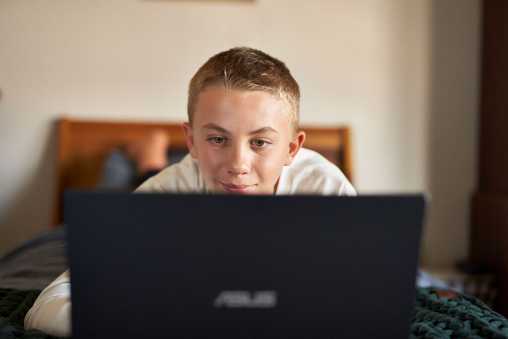 An elementary school student using Microsoft Forms on a laptop while laying in bed at home. 