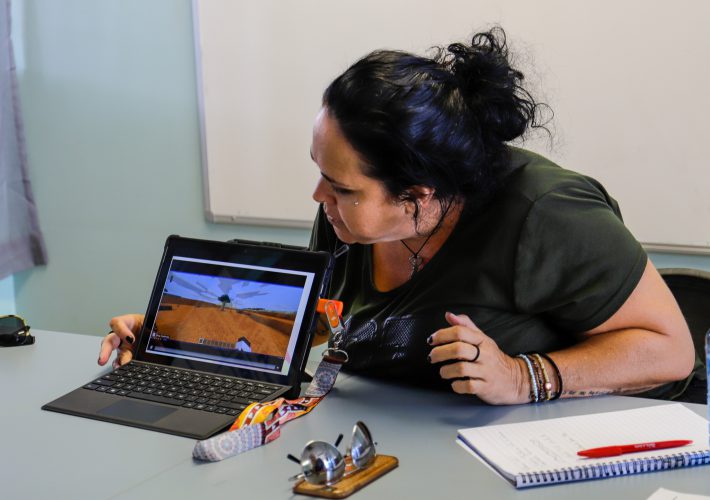 A woman sits behind a laptop displaying a tree in Minecraft: Education Edition.