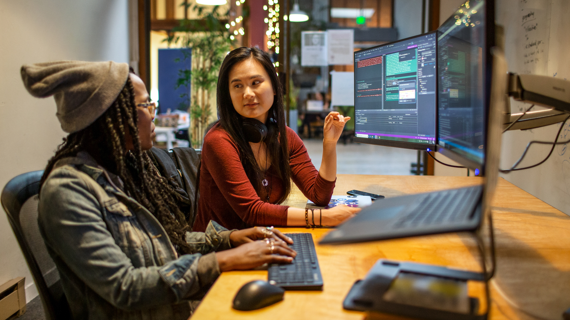 Two college students sitting at a shared desk and looking at code on computer monitors