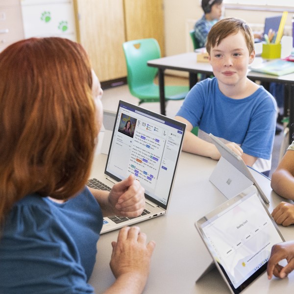 A teacher sitting at a table with students in a school classroom and engaging with them.
