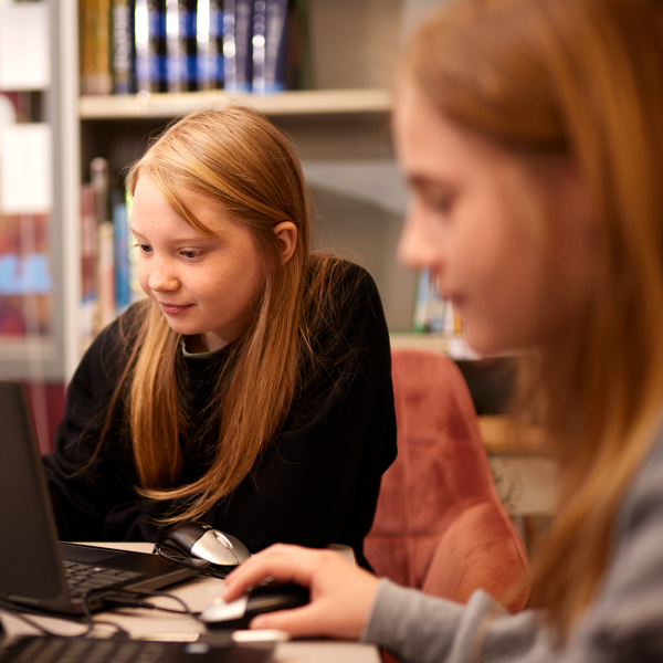 Decorative. Two students play Minecraft on their laptops in a school classroom.