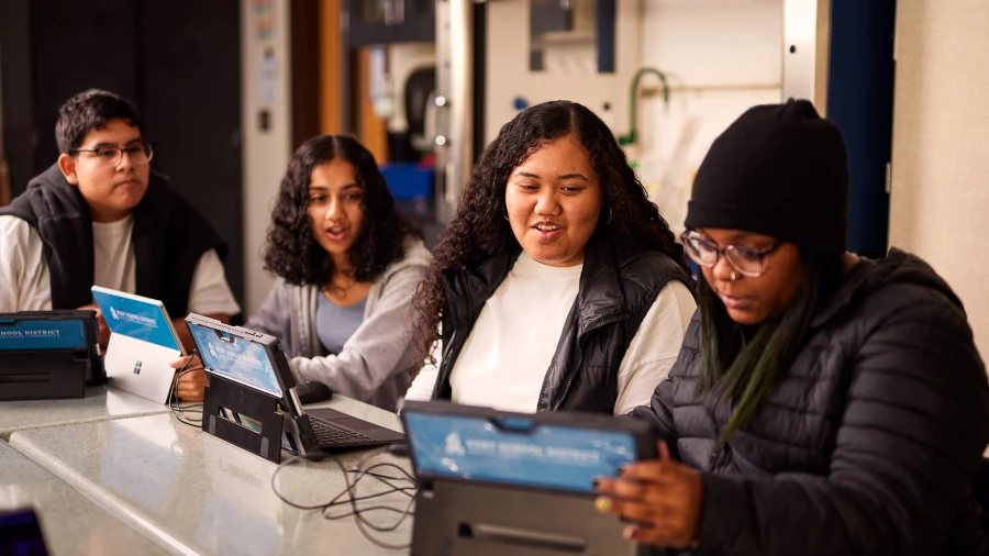 Decorative. Four high school students playing Minecraft on laptops in a school classroom.