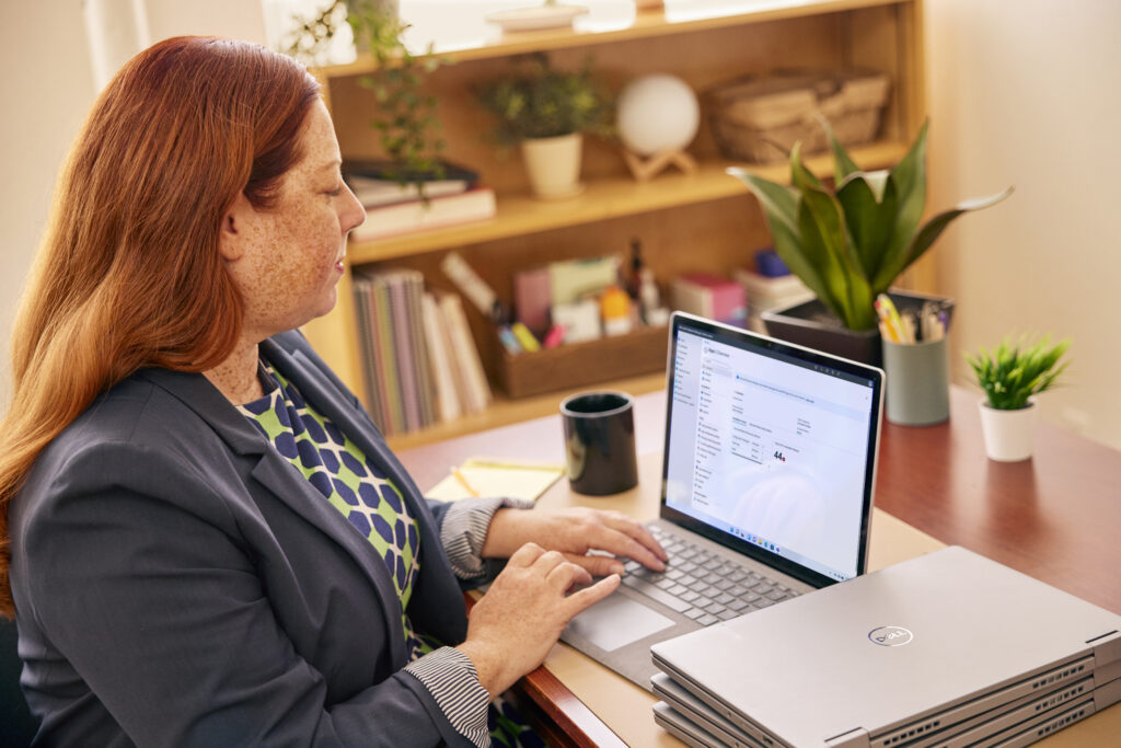 A school faculty member working on a laptop in a classroom setting.