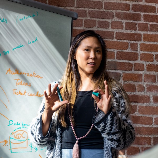 An educator teaching in front of a classroom with a marked up whiteboard in the background.