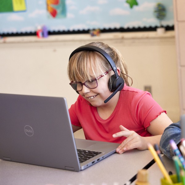 A student at a desk in a classroom interacts with Reading Coach on a laptop.