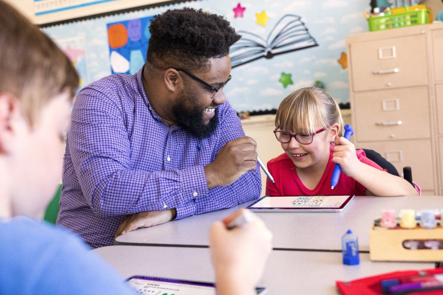 An educator engages with a student in a classroom. There’s another student sitting at the table in the foreground.
