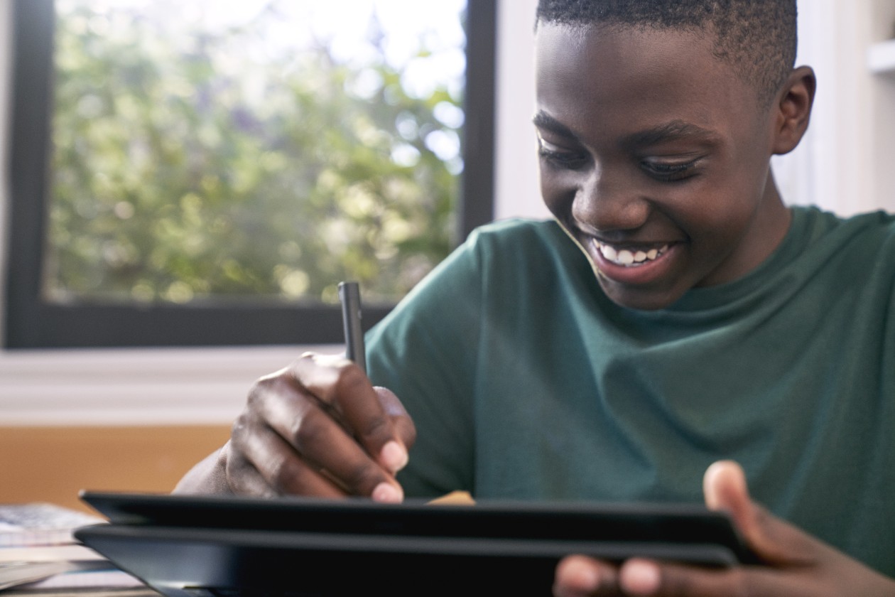 A student writing on a 2-in-1 device with a digital pen while sitting at a desk.