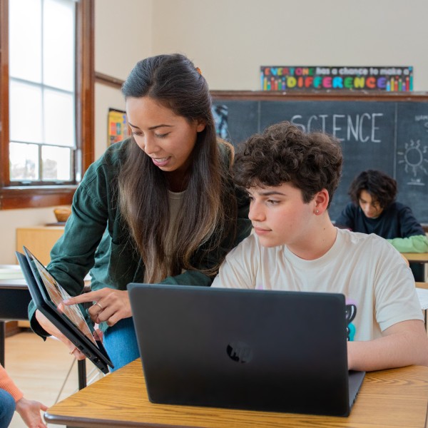 An educator in a school classroom engages with a student at the student’s desk.