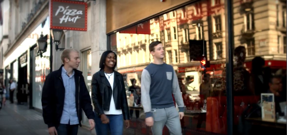 A group of people walking outside a pizza hut restaurant