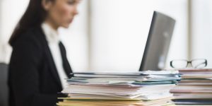 woman looking at a laptop with a pile a paperwork nearby