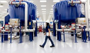 Person holding a clipboard and wearing hard hat walking through factory floor