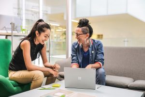 Two women conversing and using a windows laptop